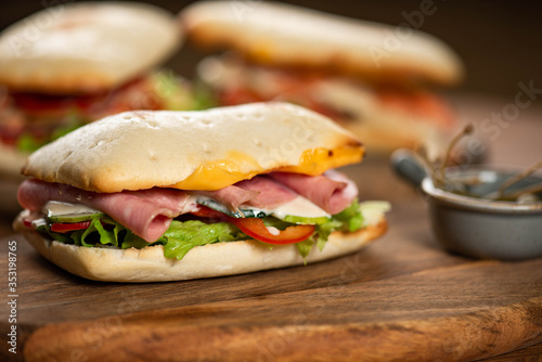 panini or hot sandwiches with beef, ham, herbs and cheese, tomatoes and red pepper on a wooden cutting board