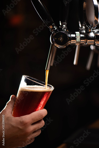 dark beer on tap beer is poured into a glass that holds man's hand on a black background, copy space