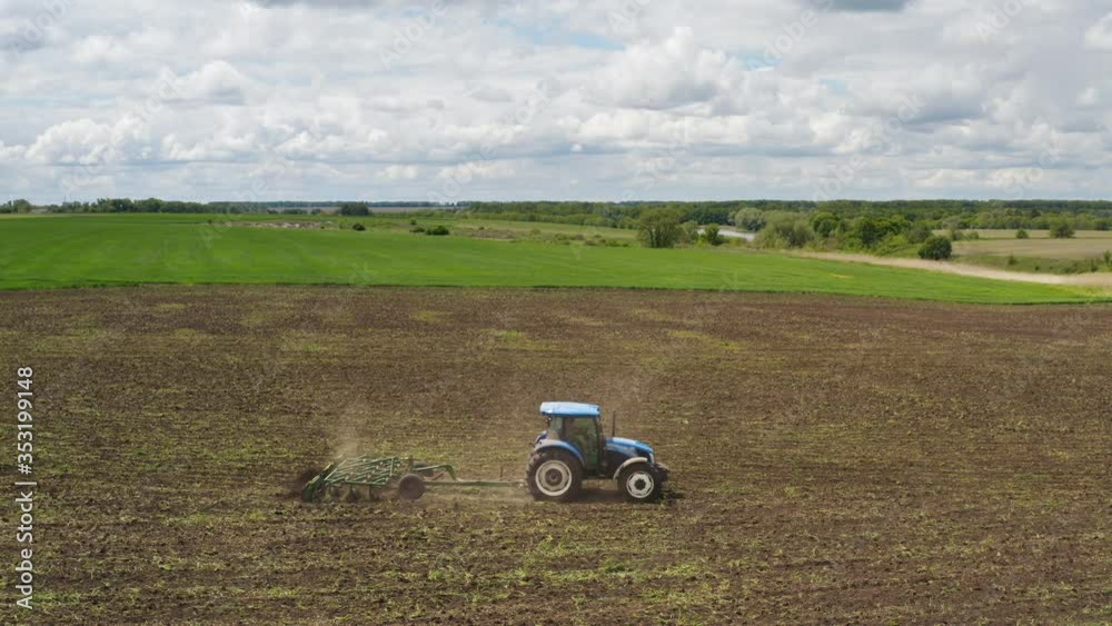 Aerial view of a farmer on a tractor with a cultivator working in the field, crust removing, soil aeration and lifting young weeds. Ground preparation before re-sowing crops Aerial view of a farmer on a tractor with a cultivator working in the field, crust removing, soil aeration and lifting young weeds. Ground preparation before re-sowing crops