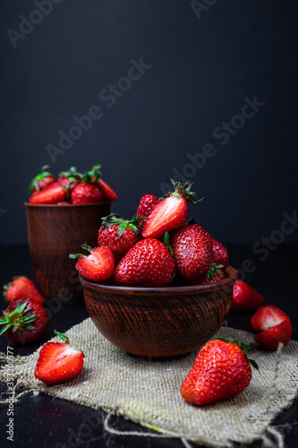 Fresh strawberry in a clay plate on dark wooden table.