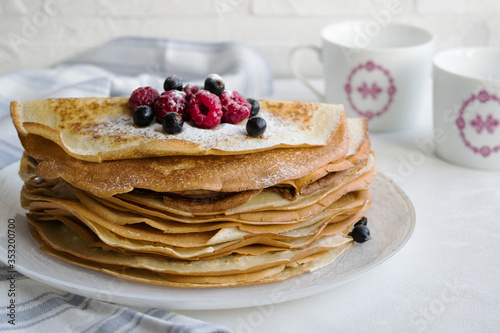 A stack of pancakes with fresh berries and icing sugar. The background is light, side view, horizontal orientation.
