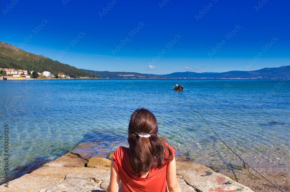 girl on the port of Muros in Galicia, Spain having a relaxing time while she stares at the sea and a little boat
