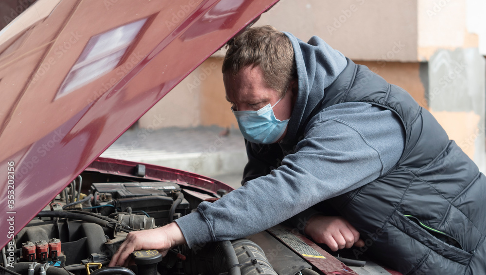 Mechanic in a protective medical mask checks a car engine Mechanic in a protective medical mask checks a car engine