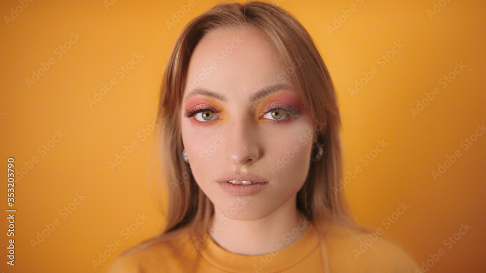 Portrait of young caucasian fashionable woman with green eyes, long eyelashes and make up isolated on the orange background. Beauty concept Portrait of young caucasian fashionable woman with green eyes, long eyelashes and make up isolated on the orange background. Beauty concept