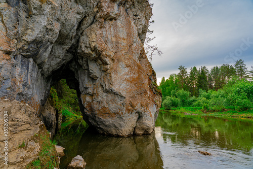 Landscape of a river bank with a rocky cliff in a horse head shape which is drinking water from the river