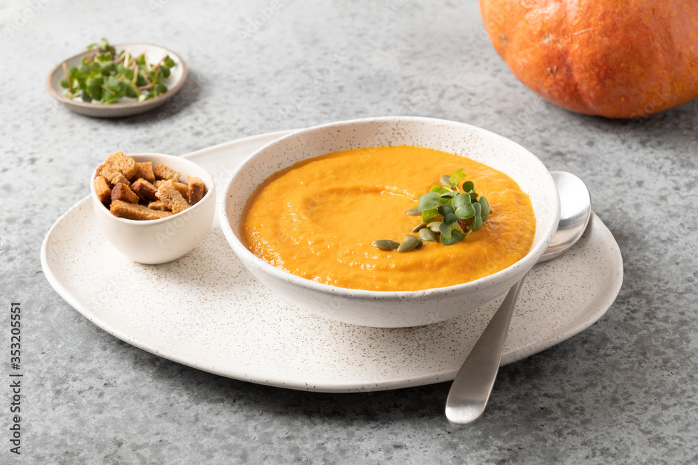 Pumpkin and carrot soup with cream garnish microgreens on grey stone background. Close up. Pumpkin and carrot soup with cream garnish microgreens on grey stone background. Close up.