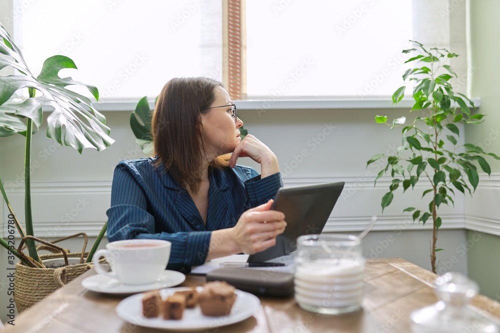 Serious mature woman working at home, using digital tablet, business notebook Serious mature woman working at home, using digital tablet, business notebook
