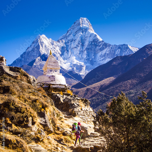 Foto A woman with a large backpack, hiking on a rocky trail past a Buddhist Stupa with a snowy Ama Dablam peak behind