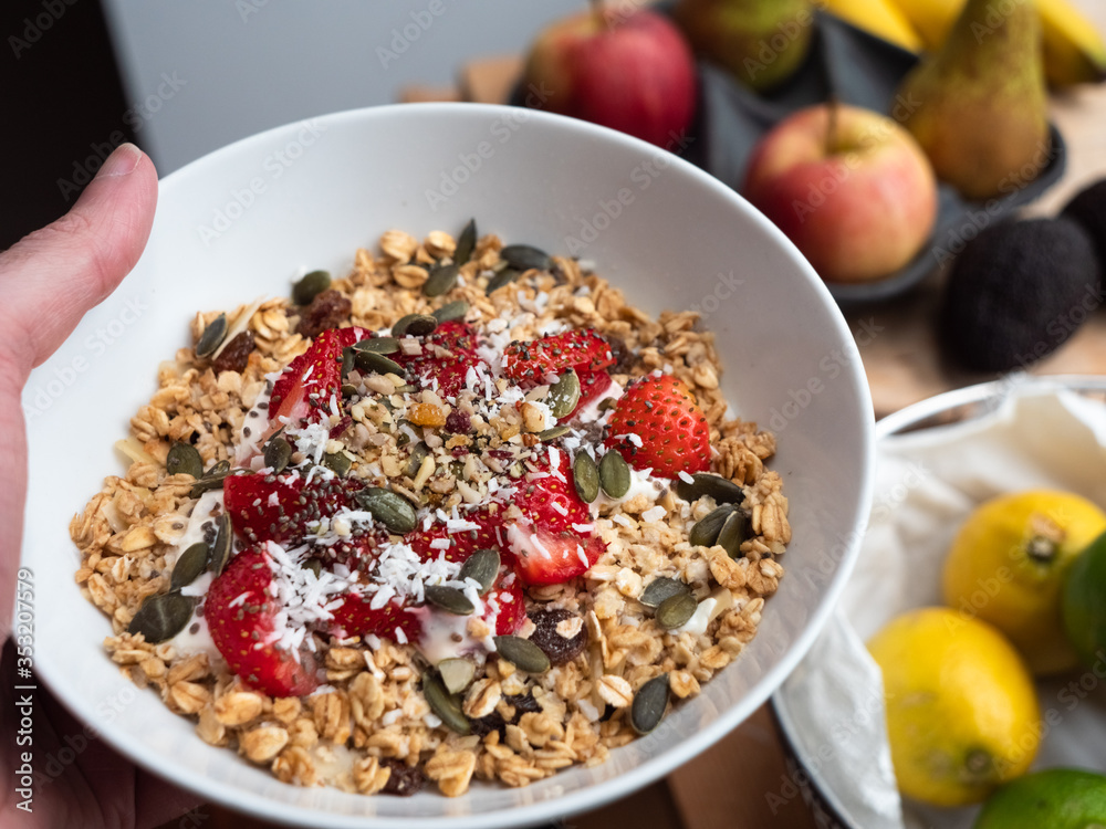 Man holding a bowl of overnight oats with strawberry, pumpkin seeds and coconut flakes on vintage teal table top with a side view style. Healthy breakfast and diet food. Man holding a bowl of overnight oats with strawberry, pumpkin seeds and coconut flakes on vintage teal table top with a side view style. Healthy breakfast and diet food.