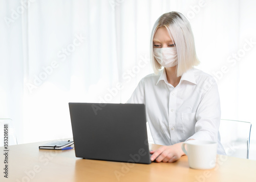  A young girl works with a laptop at home or in the office. antiviral mask.