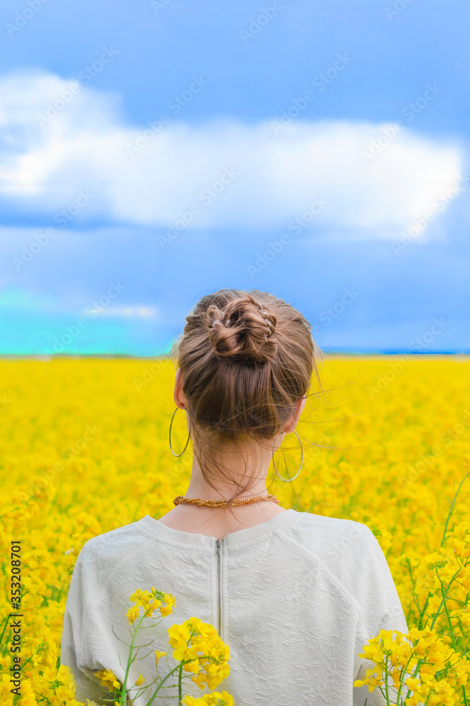 Fototapeta premium Brunette girl in rapeseed field summer time, back shot blue sky background. Happy beautiful young woman on blooming rapeseed field full of joy and happiness. Concept of freedom and childhood