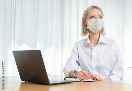  A young girl works with a laptop at home or in the office. antiviral mask.