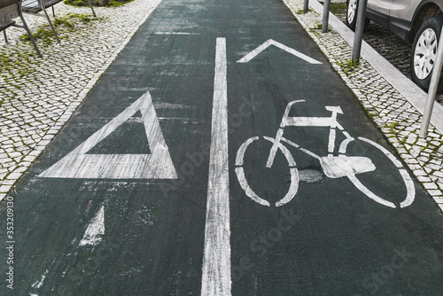 Wide-angle view of a road marking sign on asphalt on a bicycle lane and the running track, dividing line in the center, paving-stone on sides