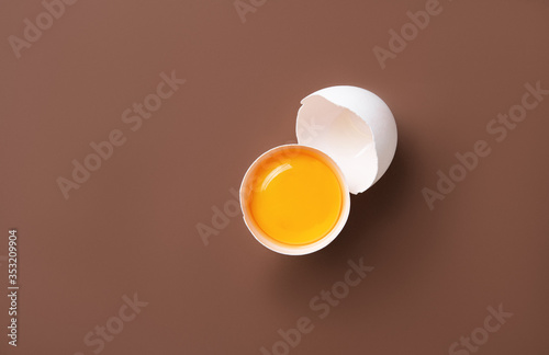 a fresh egg broken into two halves on a brown background. Top view and copy space
