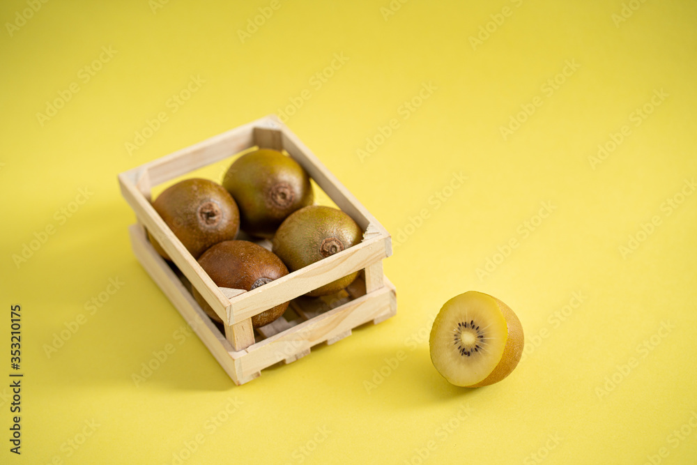 Sun gold kiwi in wooden fruit crate on a yellow background Sun gold kiwi in wooden fruit crate on a yellow background