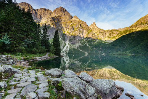 Amazing landscape with high rocks and illuminated peaks, stones in mountain lake(Morskie Oko), reflection at morning sunrise. Concept awakening and harmony with nature. Tatra National Park. Europe.
