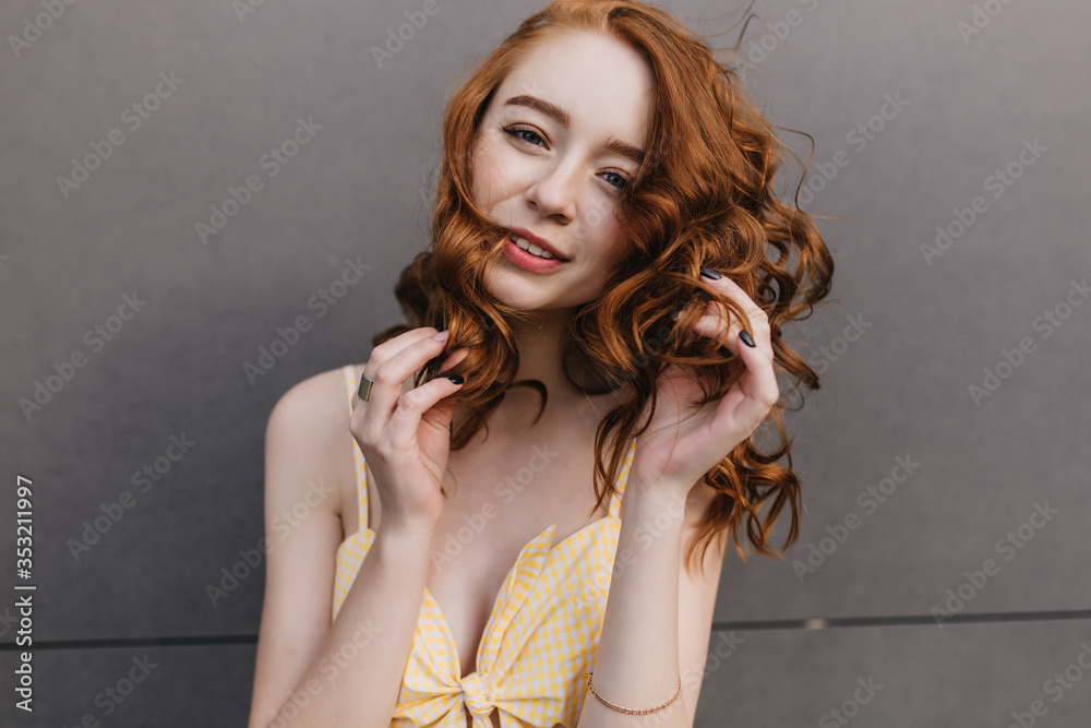 Funny ginger girl posing on gray background. Photo of elegant red-haired young woman with wavy hairstyle.