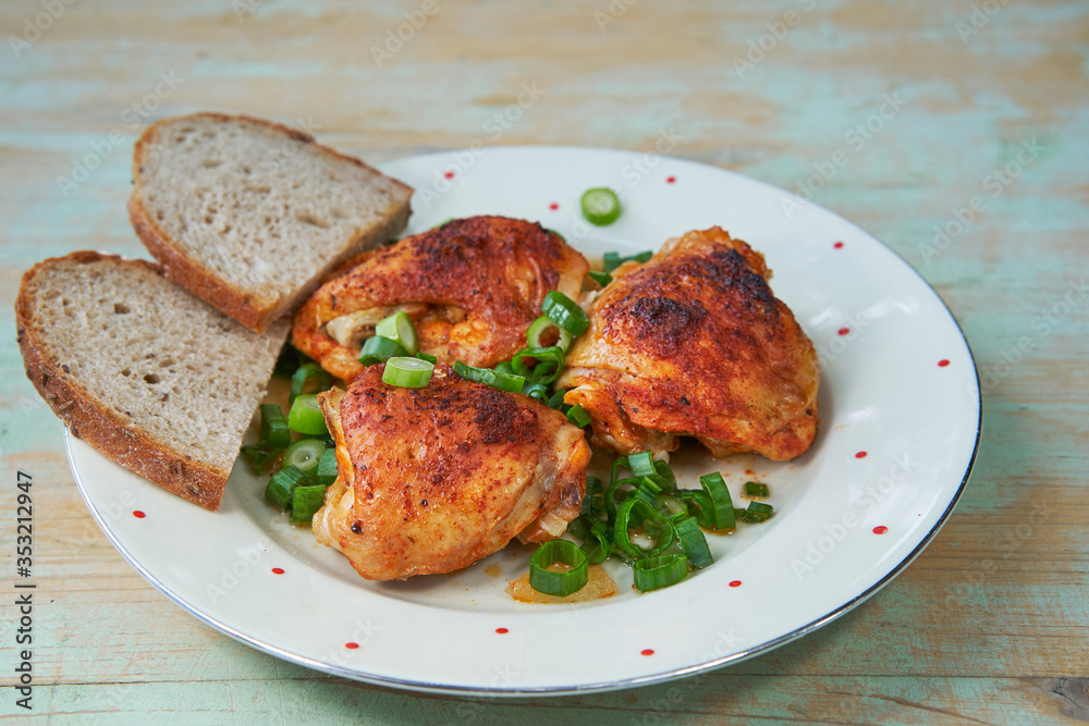 Top view on roasted hot spicy chicken leg pieces sprinkled with chopped spring onion and two slices of rustic bread. Served on the vintage porcelain plate. Tasty and juicy delicious light dietary dish