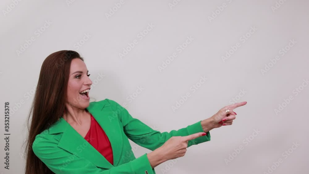 Young Attractive Woman Brunette In Purple Stylish Dress, With Green Jacket On White Background, Happy Female Smiling, Shows Direction Forefinger. The Concept Of Happy, Successful People Young Attractive Woman Brunette In Purple Stylish Dress, With Green Jacket On White Background, Happy Female Smiling, Shows Direction Forefinger. The Concept Of Happy, Successful People