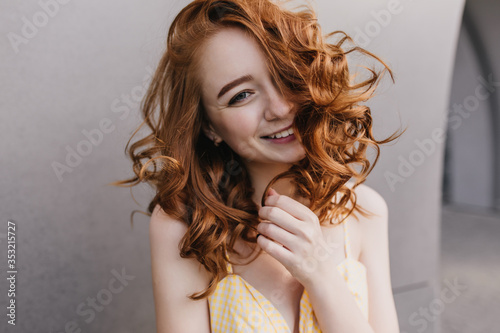 Close-up portrait of positive glamorous woman with red hair. Smiling caucasian girl expressing happiness on gray background.