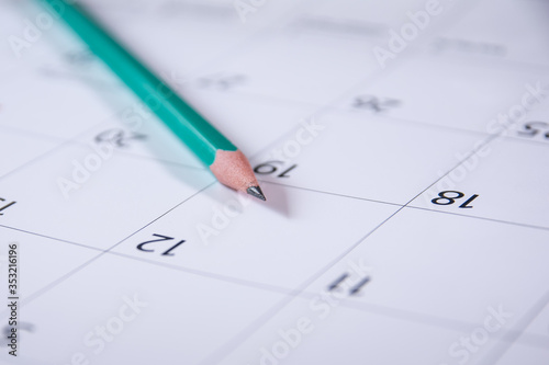 a green slate pencil lies on an opened blank calendar. Work planning. © Marina Gordejeva