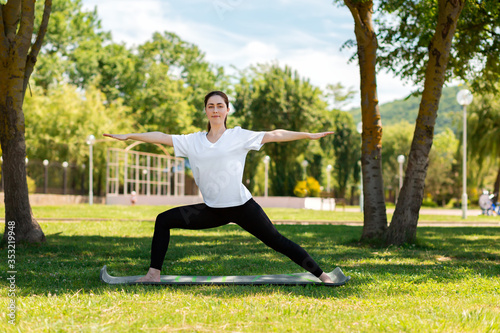 Yoga. A young smiling woman stands in a warrior's asana, doing yoga in a Park on the grass. The concept of healthy lifestyle and sports