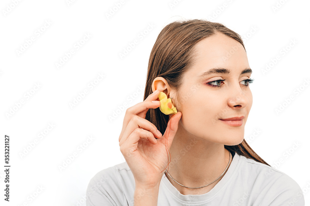 Individual earplugs for women. Woman holding customized earplug near the ear, on white background Individual earplugs for women. Woman holding customized earplug near the ear, on white background