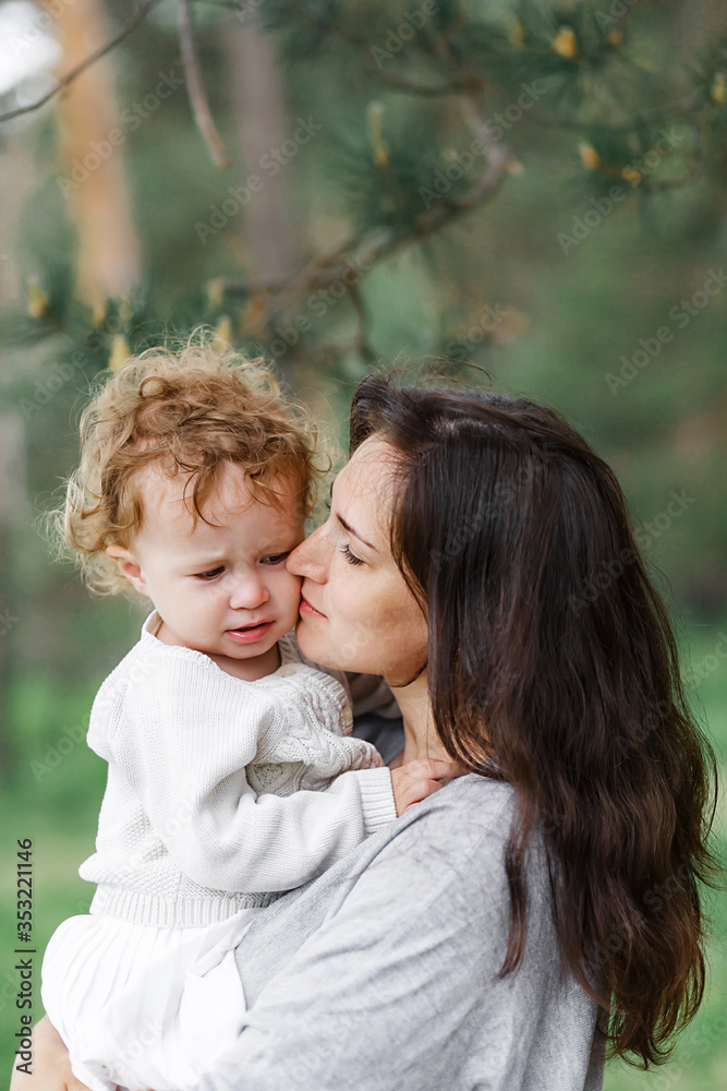 young attractive girl with long hair, brunette, in clothes of neutral colors, stands in the summer forest with her daughter little baby girl young attractive girl with long hair, brunette, in clothes of neutral colors, stands in the summer forest with her daughter little baby girl