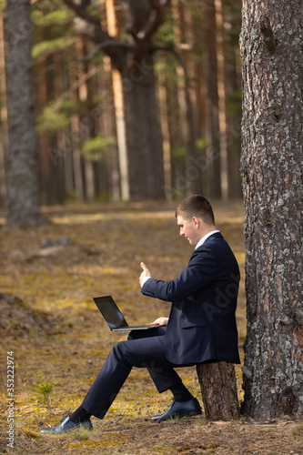 freelancing in nature. a man works on a laptop in a pine forest. businessman's office in the park.