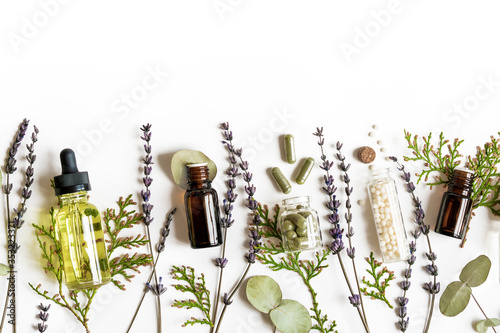 Homeopathy eco alternative medicine concept - classical homeopathy pills, thuja, eucalyptus, lavender essential and aroma oil and healing herbs and on white background. Flatlay. Top view. Copyspace