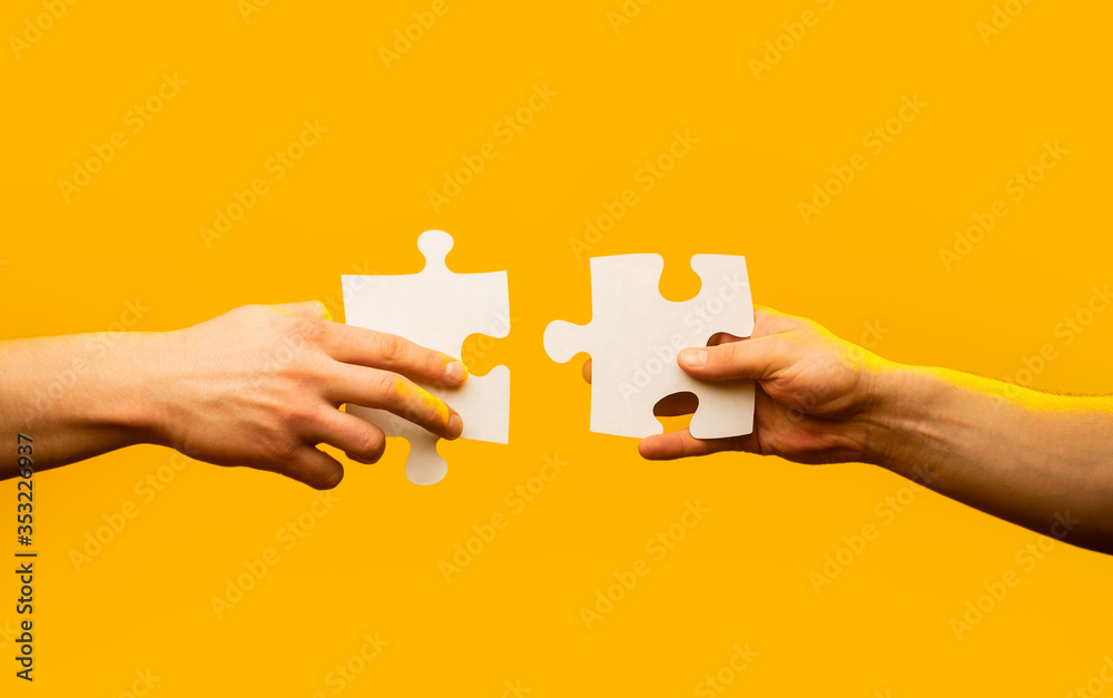 Two hands trying to connect couple puzzle piece on yellow background. Teamwork concept. Holding puzzle. Closeup hand of connecting jigsaw puzzle. Business solutions, success and strategy concept Two hands trying to connect couple puzzle piece on yellow background. Teamwork concept. Holding puzzle. Closeup hand of connecting jigsaw puzzle. Business solutions, success and strategy concept