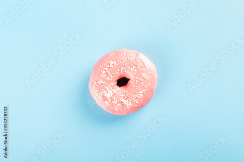 Donut with pink icing and coconut pastry topping on blue background. Top view
