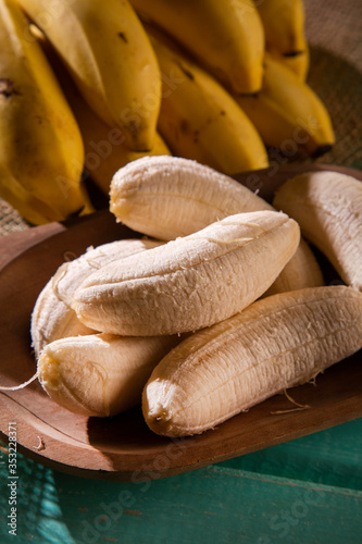 A banch of bananas and a sliced banana on wood background.