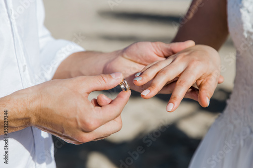 Bride and groom exchanging wedding rings close up during symbolic nautical decor destination wedding marriage on sandy beach in front of the ocean in Punta Cana  Dominican republic 