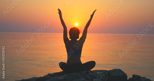 Girl practices yoga near the ocean during sunrise time, lotus pose, sun salutating photo