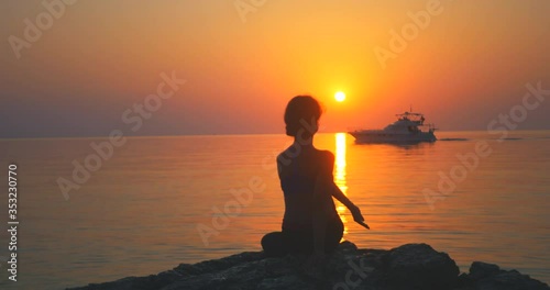 Young woman stretching near the ocean during sunrise time, lotus pose, focus on the woman, changing focus photo