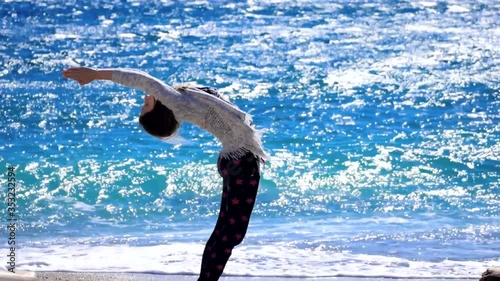 Young woman amateur making sun salutating excercise near the sea in windy weather, her hair fluttering in the wind. photo