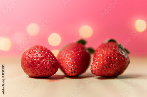 Three fresh strawberries on pink background with bokeh lights. Beautiful photo of strawberries. Vegan fruit ingredients for diet. Summer vibes picture