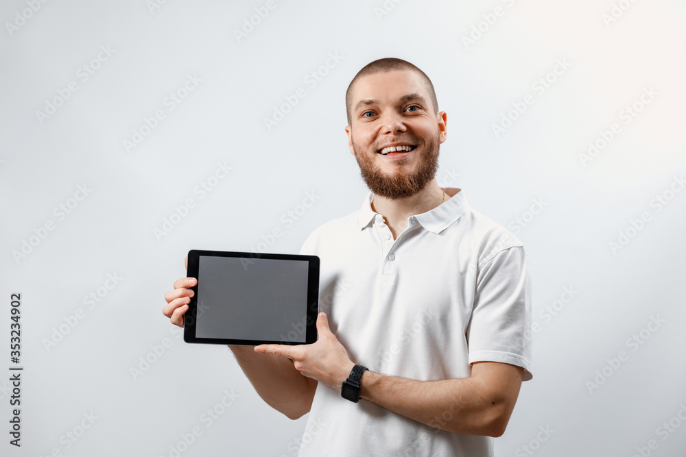Portrait of a handsome happy bearded man in a white t-shirt shows a tablet on a white background. isolated, emotions Portrait of a handsome happy bearded man in a white t-shirt shows a tablet on a white background. isolated, emotions