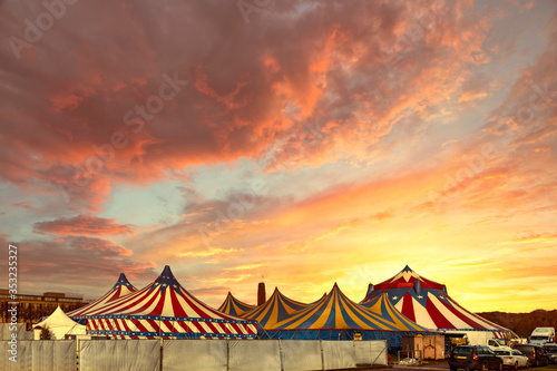 Red and white circus tents topped with bleu starred cover against a sunny blue sky with clouds