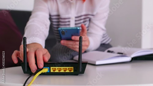 Closeup of a wifi router and a redhead woman using smartphone on living room at home office.