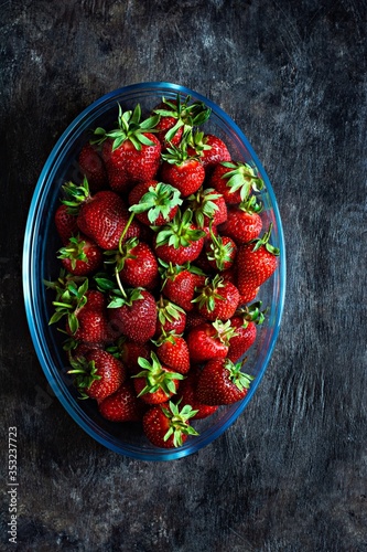 Fresh ripe strawberries in a glass dish on a dark background, top view.