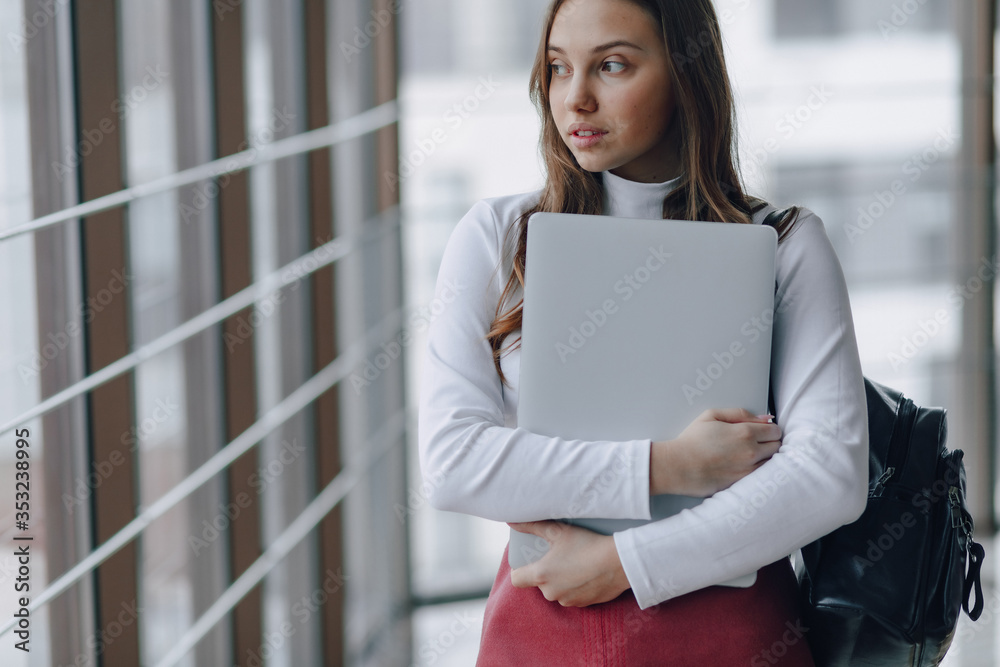attractive girl walks in a bright corridor with laptop and things in airport terminal or office. travel atmosphere or alternative work atmosphere. freelancer student travels to business meeting. attractive girl walks in a bright corridor with laptop and things in airport terminal or office. travel atmosphere or alternative work atmosphere. freelancer student travels to business meeting.