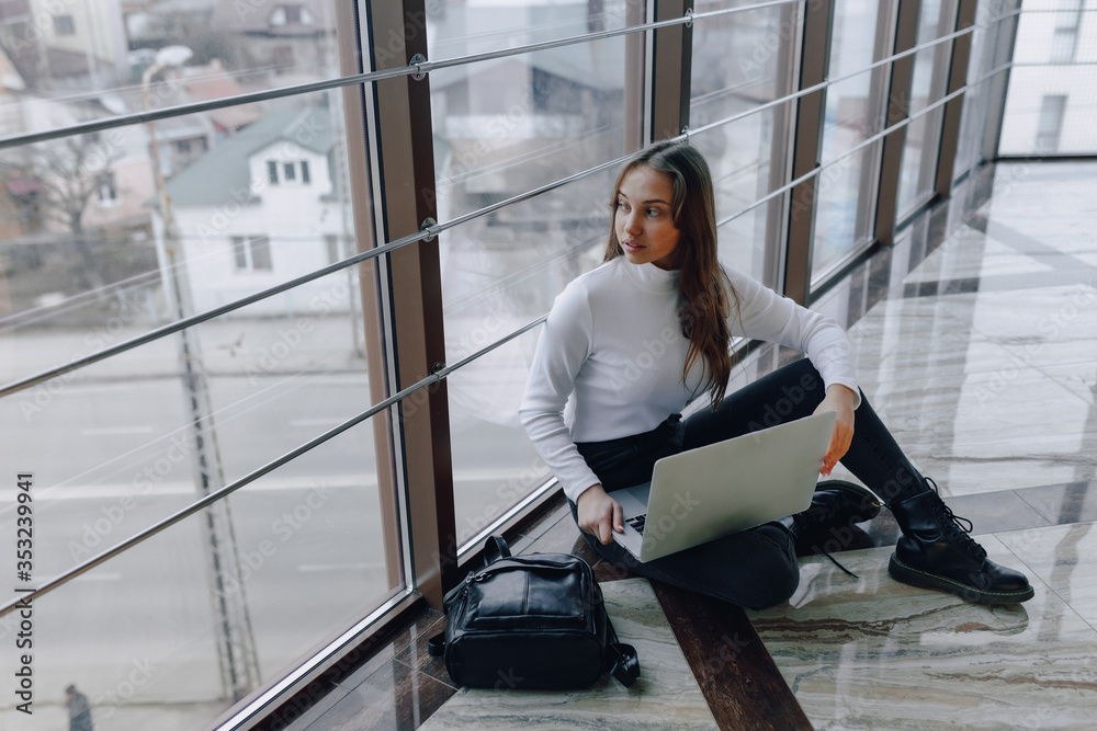 attractive girl working with laptop and things in airport terminal or office on floor. travel atmosphere or alternative work atmosphere. freelancer student travels to business meeting.