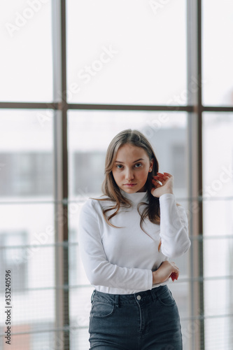 attractive girl on the background of the window shows different emotions and mood. girl on a light background indoors.