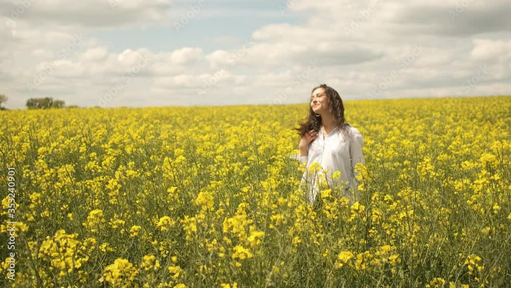 Cheerful girl of Caucasian appearance in rapeseed. Walks across the field in yellow flowers Cheerful girl of Caucasian appearance in rapeseed. Walks across the field in yellow flowers