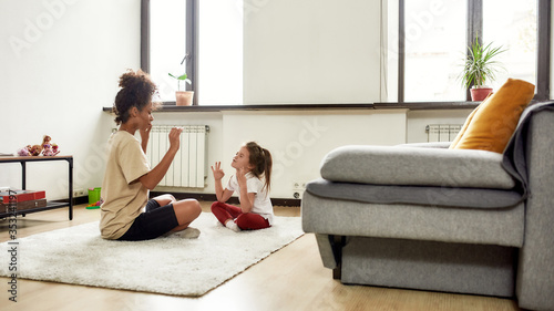 Healthcare. African american woman baby sitter and caucasian cute little girl doing yoga at home