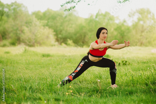 Young woman practising yoga in the open air in the nature on the grass on the sunny day. Outdoor sports. Exercises for tonus, flexibility and power. Soft focus