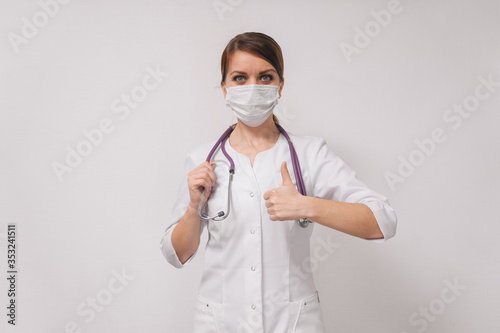 A young doctor woman in a medical mask shows that everything is fine. The concept of recovery  thumbs up