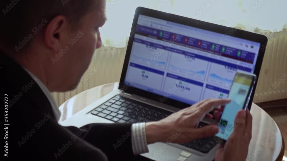 Teleworking businessman analysing stock market exchanges with laptop and phone Teleworking businessman analysing stock market exchanges with laptop and phone